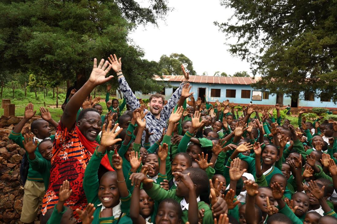 Chris celebrating with a crowd of cheering schoolchildren at an outreach
