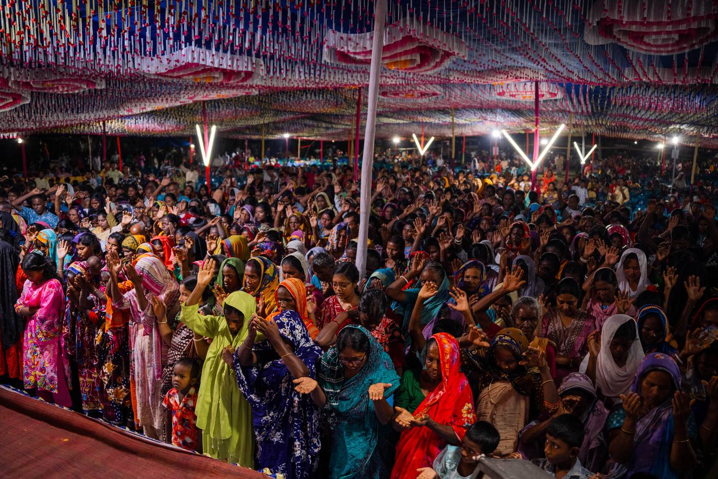 A crusade crowd with hands raised under the tent in Bangladesh